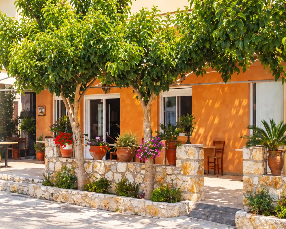 The orange front of Barbantonis taverna, with trees, flower pots and a stone courtyard